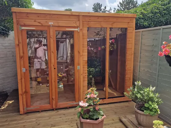 Timber summer house with large glass doors and potted flowers on a garden deck